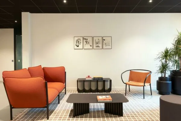 Stijlvol ingerichte wachtruimte met moderne oranje en leren stoelen, een zwarte salontafel en abstracte kunst aan de muur.